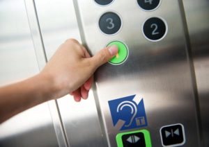 A person pressing an elevator button. Beneath is the hearing loop symbol