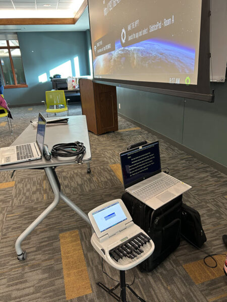 Front of meeting room with stenographer's machine, laptop and projection screen