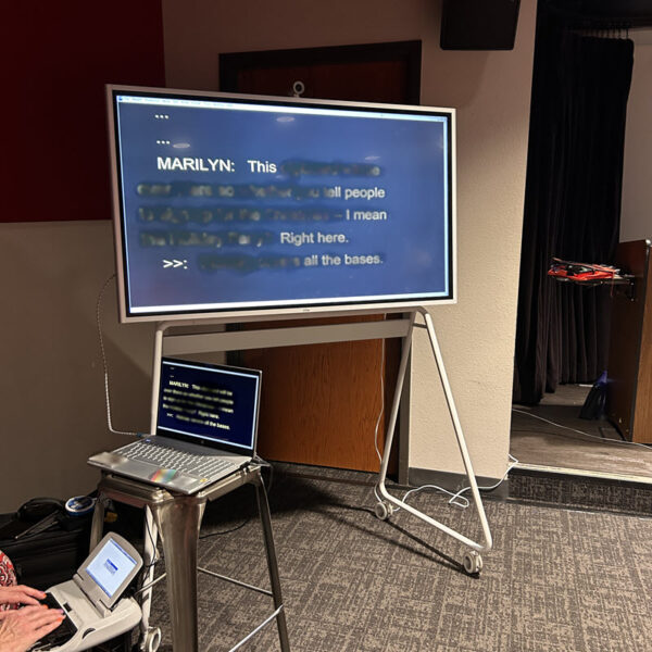 A CART provider, stenography machine, laptop, and "Vibe" board on wheels.