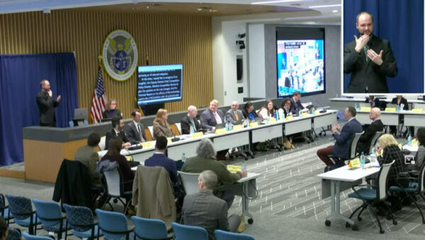 FCC committee meeting. CART is displayed on a screen behind the committee. To the right is second screen showing the video feed with captions overlaid