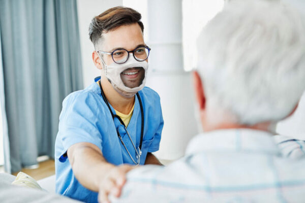 photo of a medical provider wearing a clear mask, talking with a patient with white hair