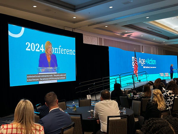 Audience looking at two screens during plenary conference session, Captions are at the bottom of the screen.