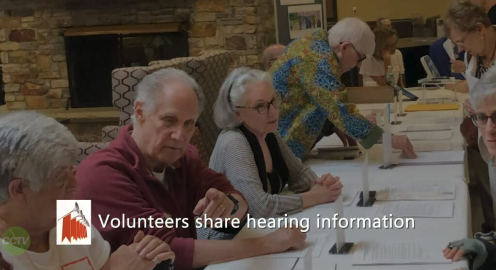 volunteers share hearing information. 4 people sitting behind a long table and sharing info