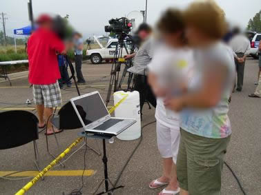 CART displayed on stand at community wildfire debrief. Two people are viewing the captions. In the background is the news media